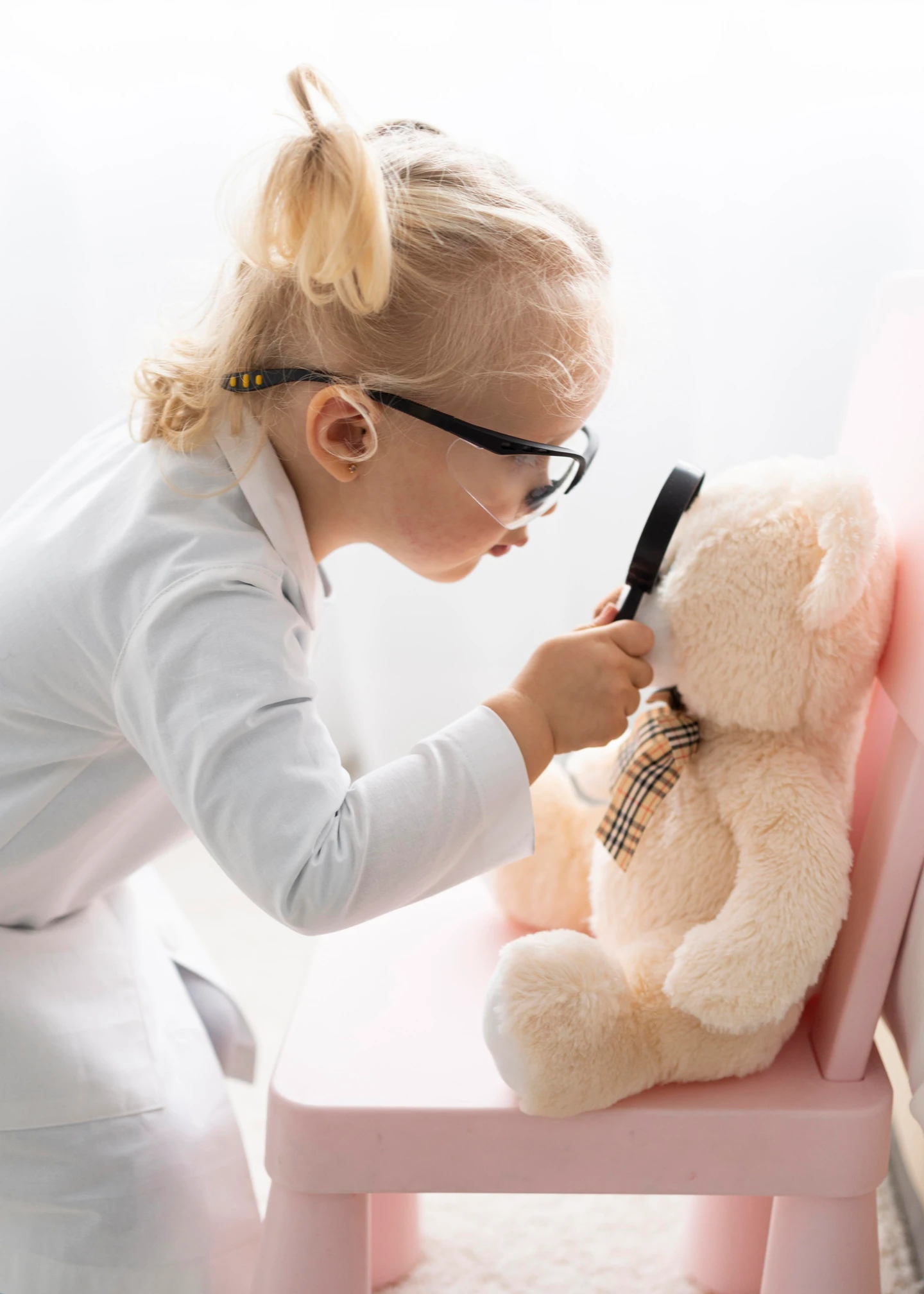 Kind mit Schutzbrille, das eine Lupe vor einem Teddybäre hält